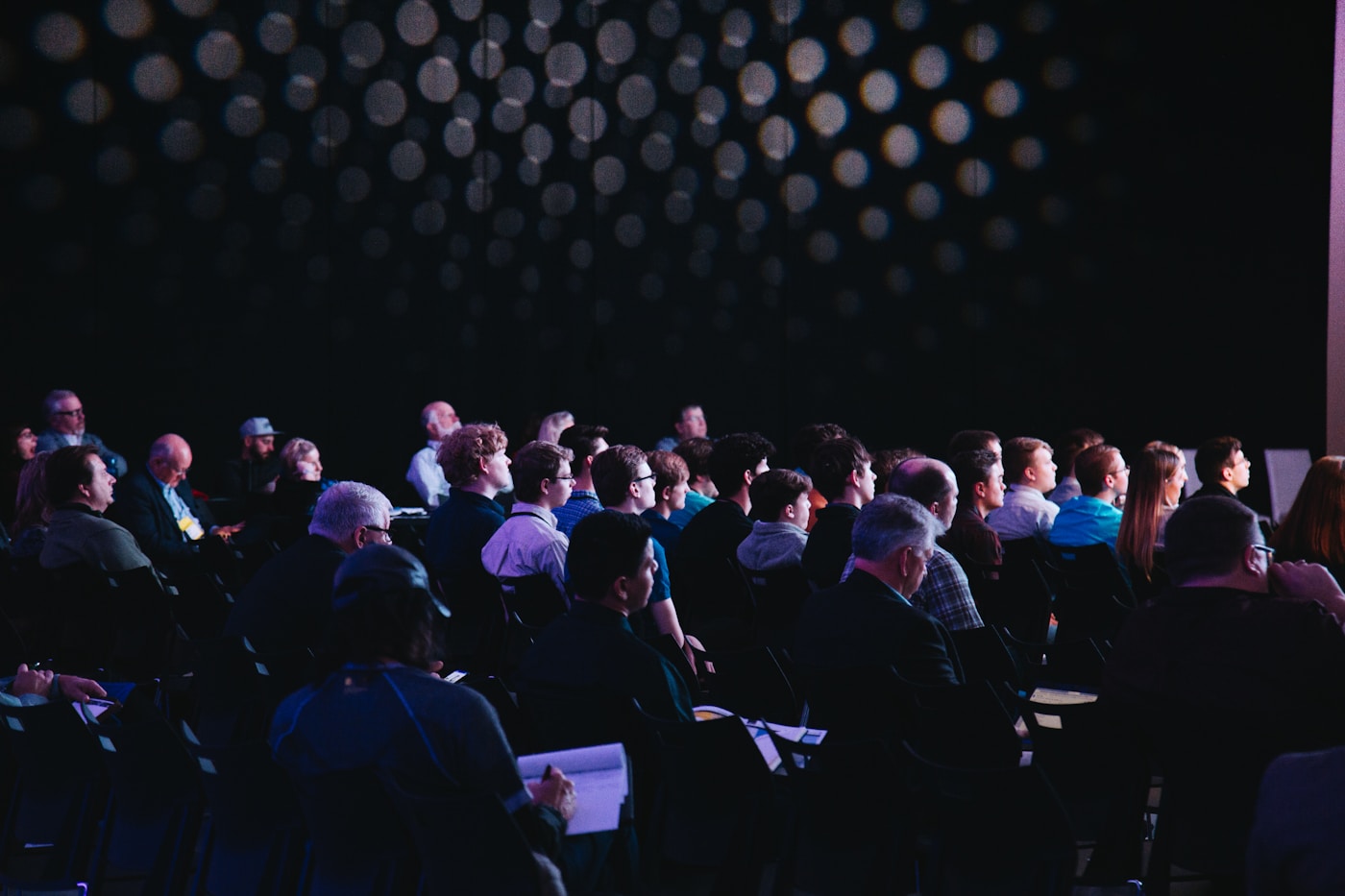 A seated audience watching a conference session in a darkened hall