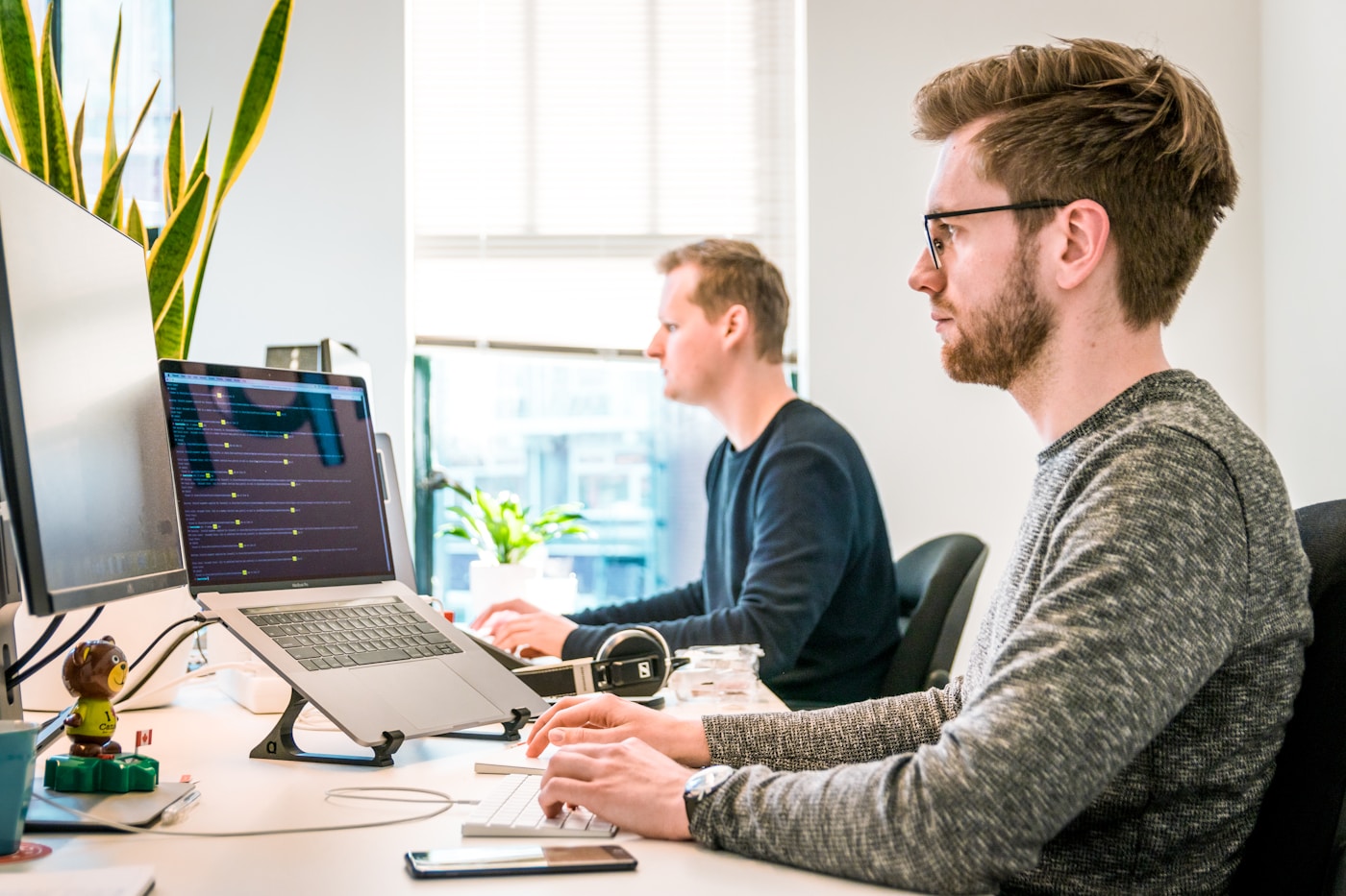 Two analysts working at desks with code and tracking configuration on their screens