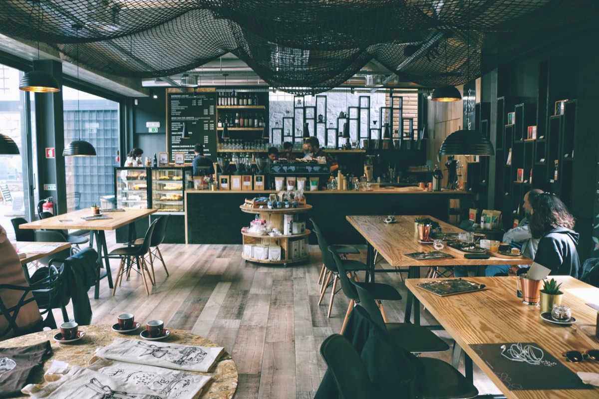 Independent cafe interior with a service counter, menu boards, and guests at wooden tables